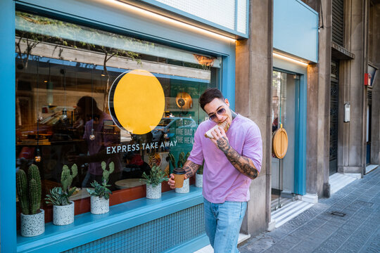 Man with takeaway coffee eating tasty sandwich on street