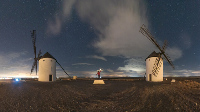 Anonymous traveler standing with torch in windmills on meadow on starry night