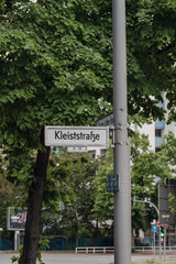 Street sign showing the street name Kleiststrasse in downtown Berlin next to green tree