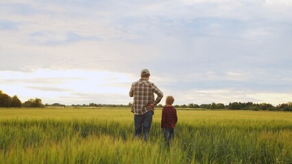 Farmer and his son in front of a sunset agricultural landscape. Man and a boy in a countryside field. Fatherhood, country life, farming and country lifestyle.