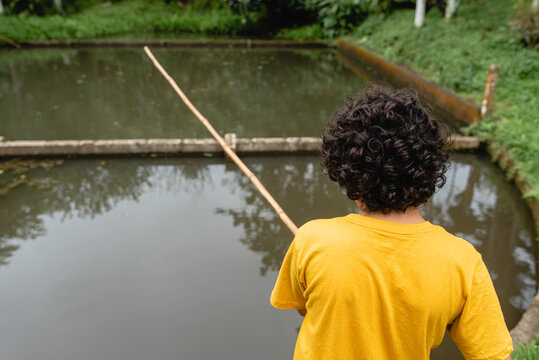 Anonymous boy fishing in pond in green garden