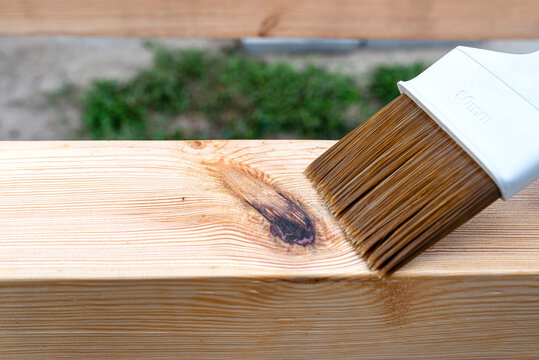 The woman impregnates raw planed wooden pine beams with dimensions of 100x100mm with a colorless impregnation.