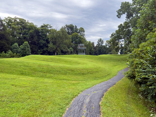 Fototapeta na wymiar Walking path at prehistoric Great Serpent Mound Earthworks snake effigy in Ohio USA. Body of snake curves along the landscape in the largest effigy mound in the world. Observation tower in background.