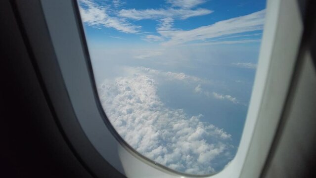 Airplane window view above clouds. Looking outside the window during an airplane travel. Flight above clouds with scenic view. Passenger looking oustide window.