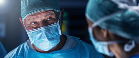 Diverse team of professional medical surgeons perform surgery in the operating room using high-tech equipment. Doctors work to save a patient in a modern hospital. Medicine, technology and healthcare.