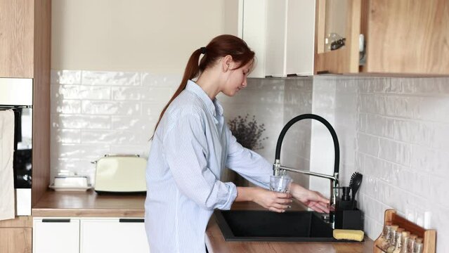 young atractive woman filling drinking glass with tap water on the kitchen and drink it. Concept of clean water at home. Water quality check concept. The concept of saving, problems with water.