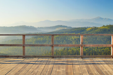 Early morning view from the wooden terrace on Carpathian mountain range. Sunbeams falling on the balcony, blue mountain peaks in the background. - obrazy, fototapety, plakaty