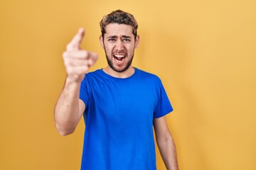 Hispanic man with beard standing over yellow background pointing displeased and frustrated to the camera, angry and furious with you