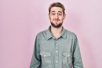 Hispanic man with beard standing over pink background puffing cheeks with funny face. mouth inflated with air, crazy expression.