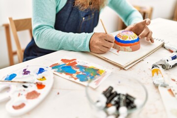 Young redhead man painting clay pottery at art studio
