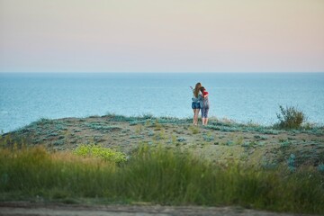 Mom and daughter are walking at sunset on the high seashore.