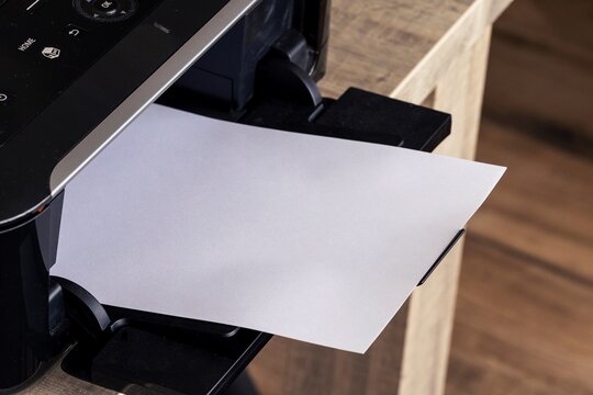 A portrait of a printer with an empty white page in its printed output tray. The blank piece of paper can be used to display some print out.