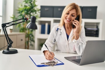 Obraz premium Middle age blonde woman wearing doctor uniform talking on the smartphone at clinic