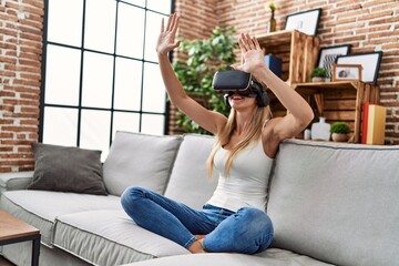 Fototapeta premium Young blonde woman playing video game using virtual reality glasses at home