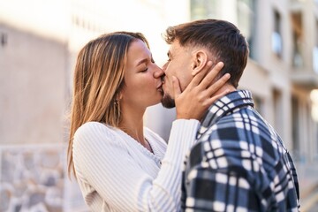 Young man and woman couple hugging each other kissing at street