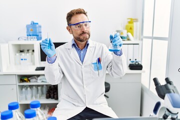 Middle age man working at scientist laboratory holding chemical products smiling looking to the side and staring away thinking.