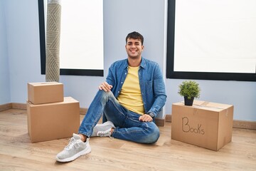 Young hispanic man sitting on the floor at new home winking looking at the camera with sexy...