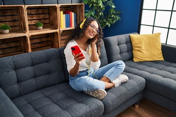 Obraz premium Young latin woman listening to music sitting on sofa at home