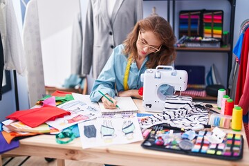 Young beautiful hispanic woman tailor drawing on notebook at tailor shop