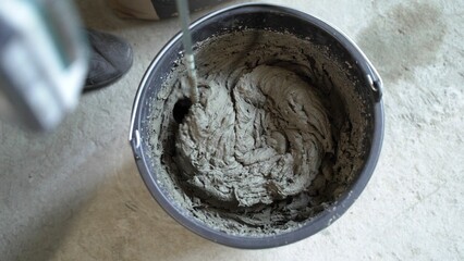 Bricklayer mixing cement in bucket. Construction worker stirs mortar.