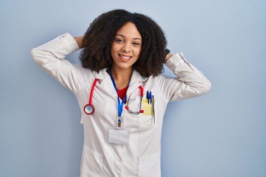 Young african american woman wearing doctor uniform and stethoscope relaxing and stretching, arms and hands behind head and neck smiling happy