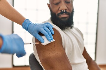 Hands of nurse woman injecting covid-19 vaccine to african amercian man at the clinic.