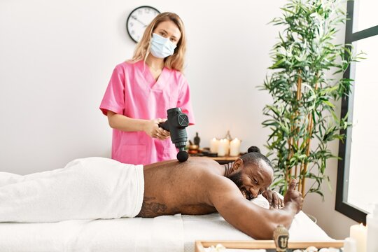 Young african american man smiling confident having back massage with percussion pistol at beauty center