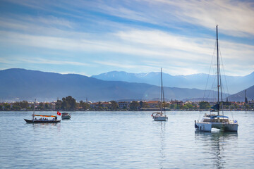 Fototapeta na wymiar Sailing yachts are anchored against the background of small town houses, mountains and blue sky