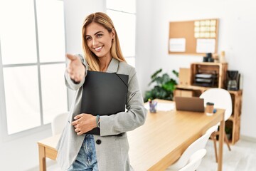 Blonde business woman at the office smiling cheerful offering palm hand giving assistance and...