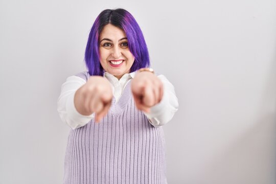 Plus size woman wit purple hair standing over white background pointing to you and the camera with fingers, smiling positive and cheerful
