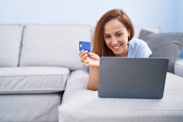 Young woman using laptop and credit card lying on sofa at home