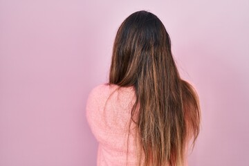 Young hispanic woman standing over pink background standing backwards looking away with crossed arms