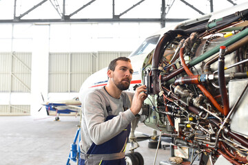 Aircraft mechanic repairs an aircraft engine in an airport hangar - 524835305