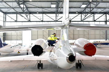 Airport workers check an aircraft for safety in a hangar - obrazy, fototapety, plakaty