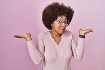 Young african american woman standing over pink background clueless and confused expression with arms and hands raised. doubt concept.