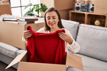 Middle age woman unpacking cardboard box sitting on sofa at new home