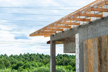 Fototapeta premium Roof trusses not covered with ceramic tiles on a single-family house under construction, visible roof elements and rafters.