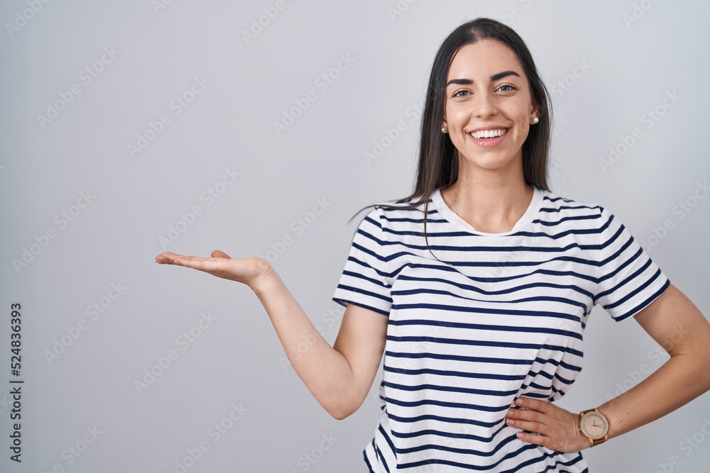 Poster young brunette woman wearing striped t shirt smiling cheerful presenting and pointing with palm of h