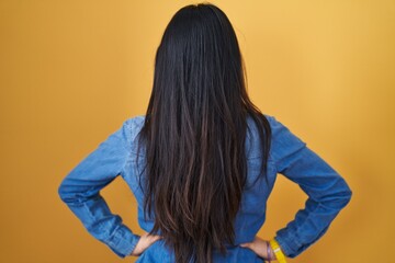 Fototapeta premium Young asian woman standing over yellow background standing backwards looking away with arms on body