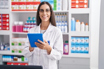 Young beautiful hispanic woman pharmacist using touchpad working at pharmacy