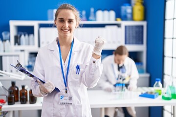 Blonde woman working at scientist laboratory screaming proud, celebrating victory and success very excited with raised arms