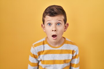 Young caucasian kid standing over yellow background afraid and shocked with surprise expression,...