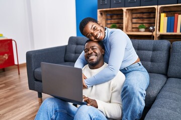 Man and woman couple using laptop sitting on sofa at home