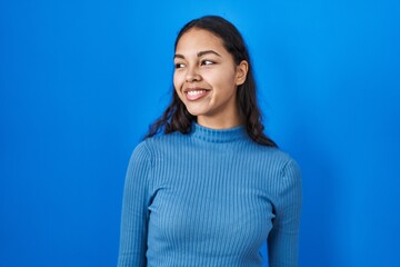 Obraz premium Young brazilian woman standing over blue isolated background smiling looking to the side and staring away thinking.