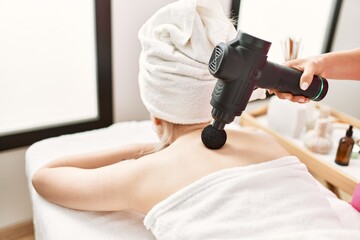 Obraz na płótnie Canvas Woman reciving back massage using gun percusion at beauty center.