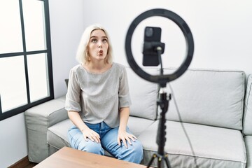 Young caucasian woman recording vlog tutorial with smartphone at home making fish face with lips, crazy and comical gesture. funny expression.