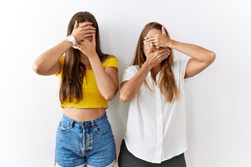 Mother and daughter together standing together over isolated background covering eyes and mouth with hands, surprised and shocked. hiding emotion