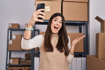 Young brunette woman working at small business ecommerce taking selfie celebrating achievement with happy smile and winner expression with raised hand