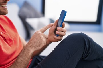 Young hispanic man using smartphone sitting on sofa at home