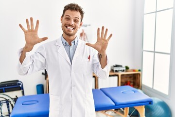 Handsome young man working at pain recovery clinic showing and pointing up with fingers number ten while smiling confident and happy.